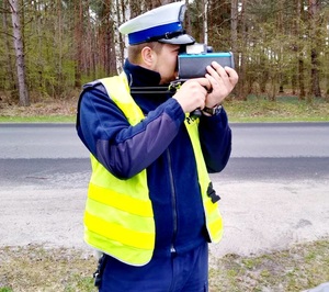 policjant przy drodze z urządzeniem do pomiaru prędkości pojazdów. w tle las