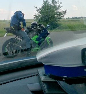 na motocyklu siedzi mężczyzna widok zza szyby pojazdu osobowego