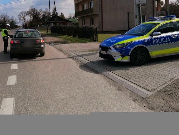 radiowóz stoi na poboczu drogi obok na drodze stoi policjant przeprowadza u kierującego osobowym pojazdem badanie stanu trzeźwości