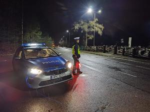 policjant stoi w nocy obok radiowozu