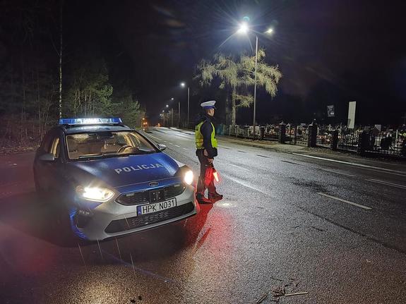 policjant stoi w nocy obok radiowozu