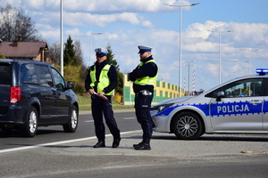 na jezdni dwóch policjantów ruchu drogowego obok osobowy radiowóz oraz osobowy pojazd koloru czarnego