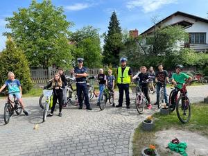 dwóch policjantów stoi na placu wśród dzieci na rowerach