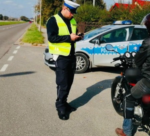 policjant wykonuje kontrolę motocyklisty za policjantem ulica obok osobowy radiowóz policyjny