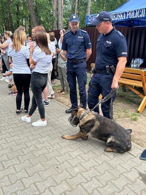 obok policjantów grupa młodzieży w plenerze przed policjantami leży duży pies