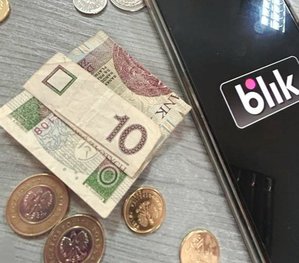 na stole leży banknot 10 złotych i monety obok telefon z wyświetlonym napisem blik