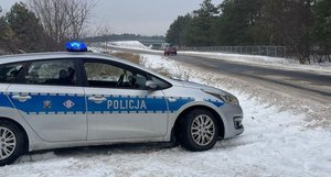 policyjny radiowóz osobowy stoi na poboczu jezdnią jedzie czerwone osobowe auto