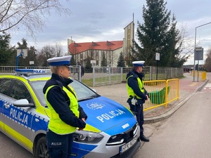 policjanci koło radiowozu stoją przy drodze