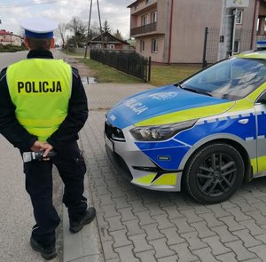 policjant stoi przy drodze obok radiowozu w ręku trzyma urządzenie do badania stanu trzeźwości