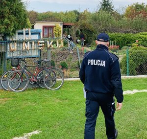 policjant idzie przez teren ogródków działkowych