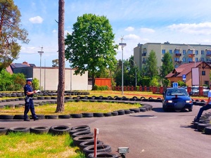 samochód osobowy z zamontowanym na masce kołem stewadra jedzie po placu manewrowym wokół którego ułożone są opony w tle policjant ruchu drogowego