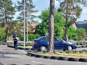 samochód osobowy z zamontowanym na pokrywie silnika kołem stewarda jeździ po placu manewrowym. W tle policjant ruchu drogowego