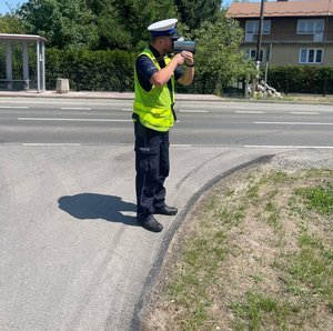 policjant mierzy przy drodze urządzeniem do pomiaru prędkości pojazdów