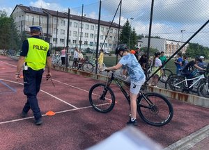 dzieci na rowerach na boisku obok policjant ruchu drogowego