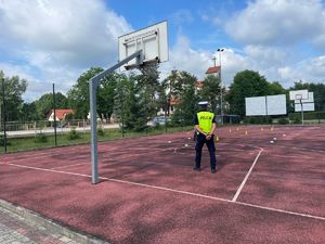 policjant ruchu drogowego stoi na boisku po którym dziecko jedzie na rowerze