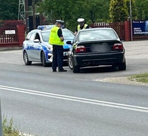 policjanci ruchu drogowego stoją obok radiowozu przed nimi stoi osobowy samochód