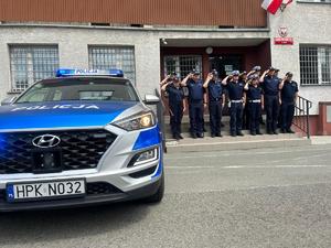 przy budynku na schodach stoją policjanci przed nimi na placu stoi radiowóz