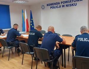 policjanci siedzą przy stole rozwiązują testy w tle napis Komenda Powiatowa Policji w Nisku