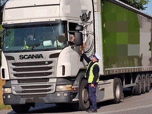 policjant podaje kierowcy samochodu ciężarowego urządzenie do badania stanu trzeźwości