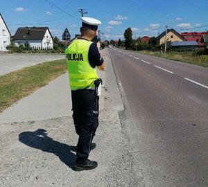 policjant stoi przy drodze mierzy prędkość pojazdów