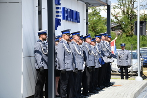 policjanci stoją w rzędzie przed budynkiem w tle sztandar