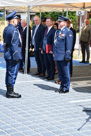 policjanci oraz osoby cywilne stoja pod zadaszeniem