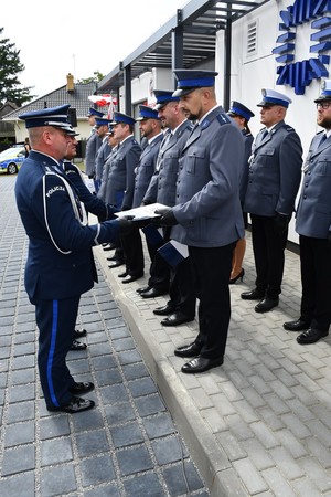 policjant wręcza policjantowi stojącemu w szeregu teczkę