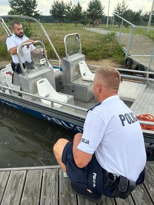 przy łodzi na wodzie obok pomostu stoją dwaj policjanci