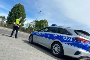 policjant stoi obok radiowozu przy drodze w ręku ma tarczę do zatrzymywania pojazdów