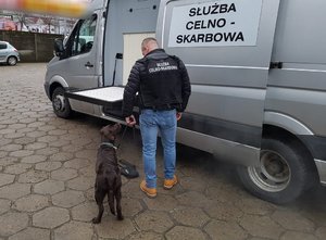 srebrny bus z napisem służba celno skarbowa przed którym stoi mężczyzna z psem