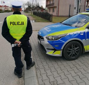 policjant ruchu drogowego stoi przy radiowozie z urządzeniem do pomiaru alkoholu w wydychanym powietrzu