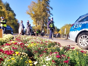 policjanci stoją na drodze przez którą przechodzą przechodnie w tle samochody