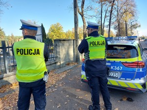 policjanci stoją przy cmentarzu w tle radiowóz