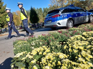 policjanci kierują ruchem na jezdni po której chodzą piesi i jadą pojazdy