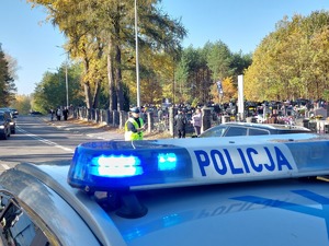 policjanci kierują ruchem na jezdni po której chodzą piesi i jadą pojazdy