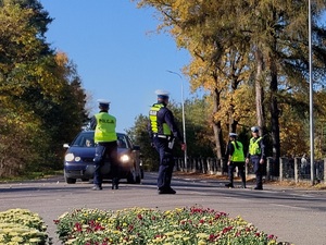 policjanci kierują ruchem na jezdni po której chodzą piesi i jadą pojazdy