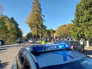 policjanci kierują ruchem na jezdni po której chodzą piesi i jadą pojazdy