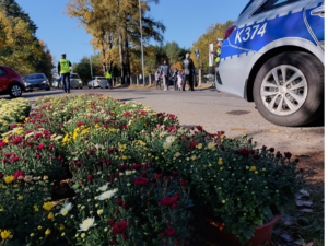 policjanci kierują ruchem na jezdni po której chodzą piesi i jadą pojazdy