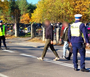 policjanci kierują ruchem na jezdni po której chodzą piesi i jadą pojazdy