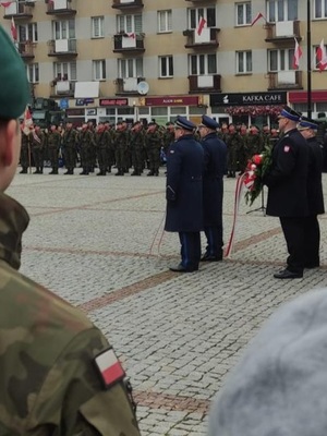 policjanci stoją w szeregu za nimi wojskowi z wiązankami kwiatów