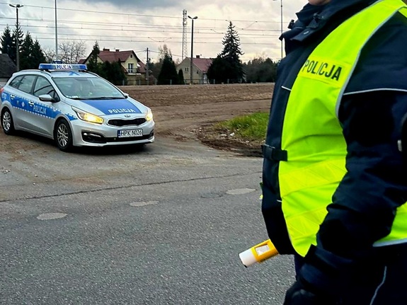 policyjny radiowóz stoi na poboczu obok policjant z alkomatem