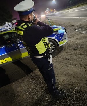 policjant prowadzi pomiar prędkości pojazdów w porze nocnej przy drodze