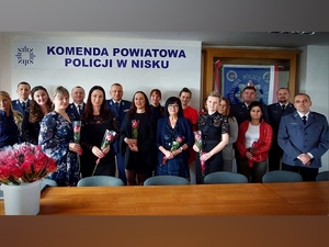 policjanci, policjantki i pracownice cywilne stoją w grupie trzymając w rękach czerwone róże na ścianie napis komenda powiatowa policji w nisku