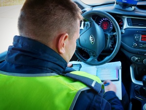 policjant siedząc w radiowozie wypisuje mandat karny