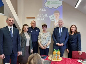 policjant stoi w grupie osób na tle ściany z napisem bezpieczny senior
