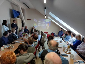 seniorzy siedza przy stołach policjant prowadzi dla nich wykład