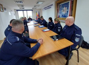 policjanci siedzą przy podłużnym stole w sali narad