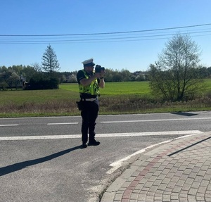 policjant prowadzi pomiar prędkości pojazdów przy drodze