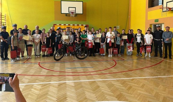 na hali sportowej stoją uczniowie z pucharami i dyplomami w towarzystwie policjantów
