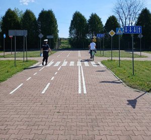 policjantka idzie obok ucznia który jedzie rowerem po miasteczku rowerowym